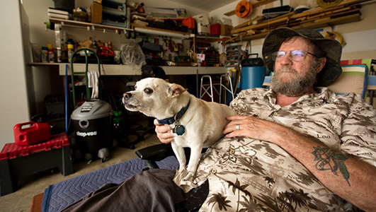 Ronnie Bishop often sits in the shade of his garage, surrounded by remnants of old hobbies he can no longer partake in, to watch the outside world. Photo by Callie Richmond for The Texas Tribune.